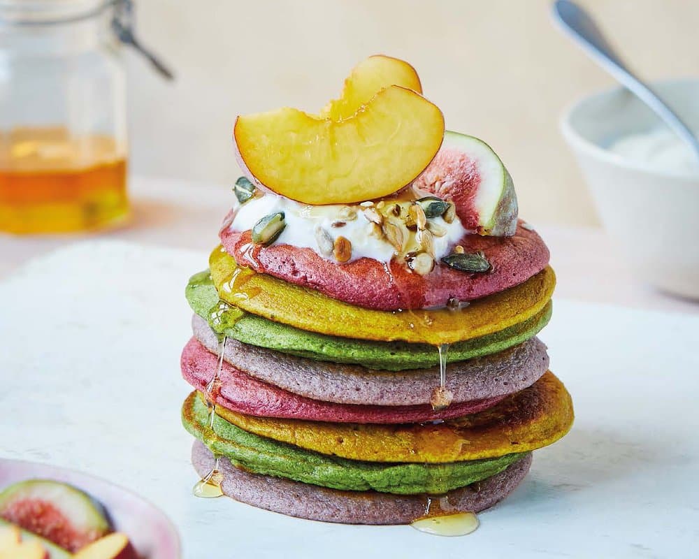 A stack of colorful pancakes with fruit toppings