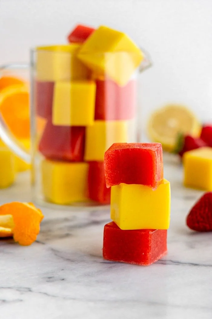 Orange and strawberry gelatin gummies stacked beside a glass jar and fresh fruit